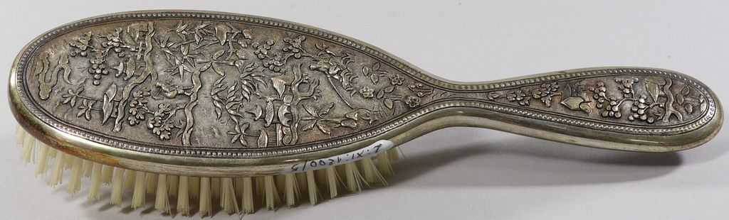 ຫີວເຮັດດ້ວຍຢາງ ໂອບດ້ວຍເງິນດ້ານຫຼັງມີຮູບເຮືອ, ຕົ້ນໄມ້ ແລະ ຄົນ.